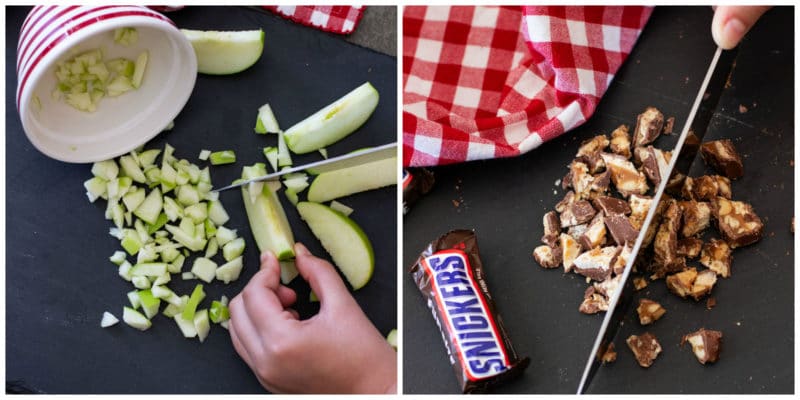 Person chopping granny smith apples and snickers bars on a black cutting board.