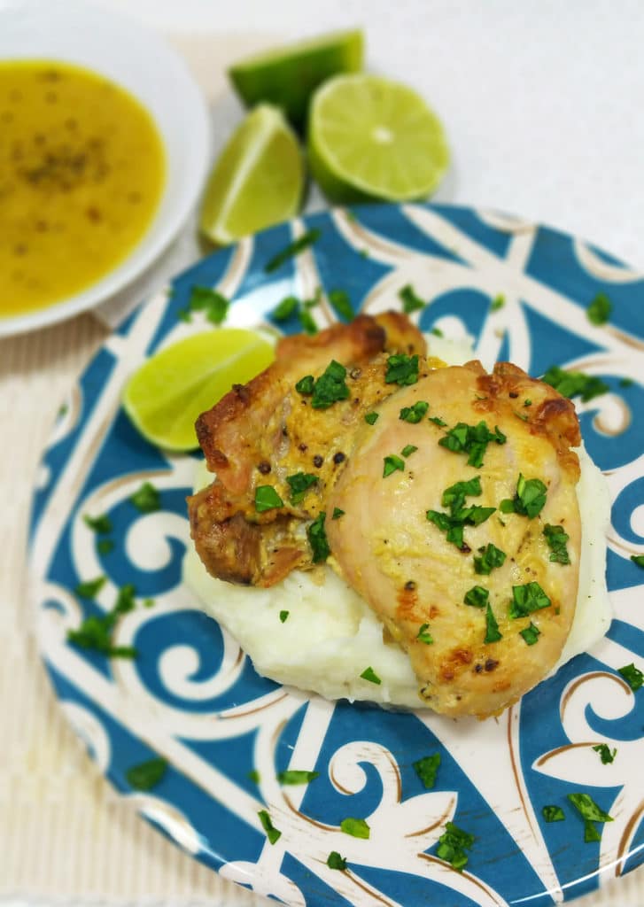 Blue plate containing Baked Chicken with Dijon Lime Sauce on top of mashed potatoes topped with fresh parsley, lime wedges and dijon mustard in white dish.