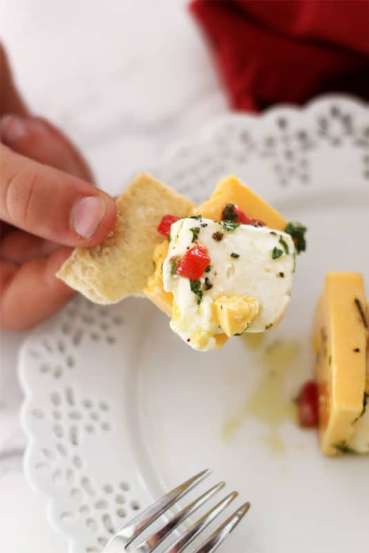 White lace plate with a pita chip covered with sharp cheddar and cream cheese, topped with pimentos, parsley, olive oil and garlic.