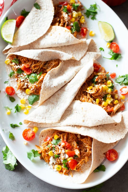 4 soft corn taco shells filled with shredded chicken, topped with cilantro, corn, and cheese.