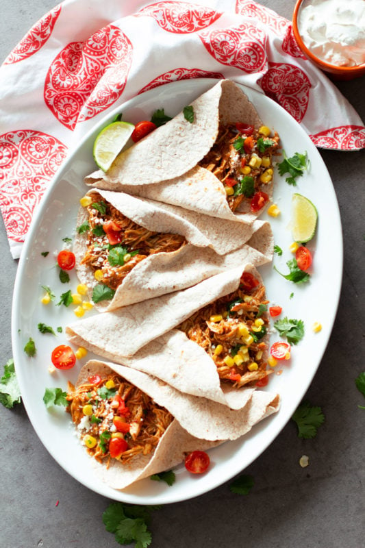 4 tacos filled with shredded salsa chicken, lime and salsa on plate.