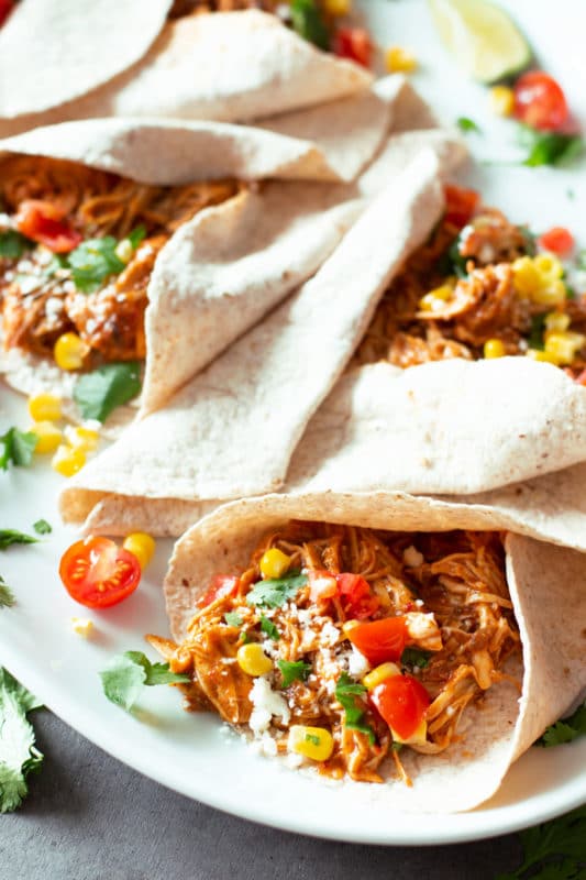 Shredded chicken taco topped with Cotija cheese, cilantro, corn, and tomatoes.