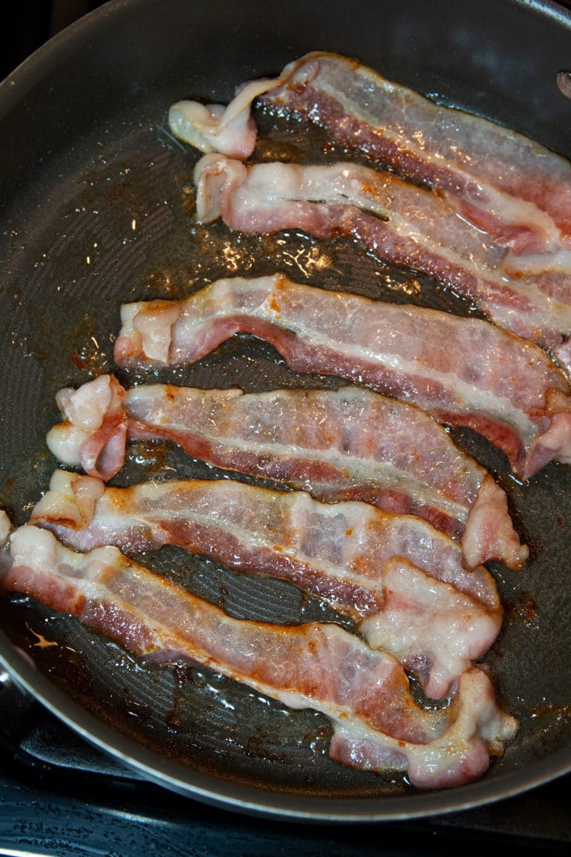 Slices of bacon frying in a skillet.
