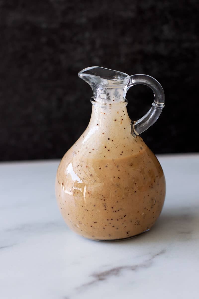 Bottle of poppy seed and balsamic dressing on white marble counter.