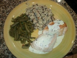 A yellow plate of two chicken breasts smothered in a mustard cream sauce with cut green beans and rice sides.