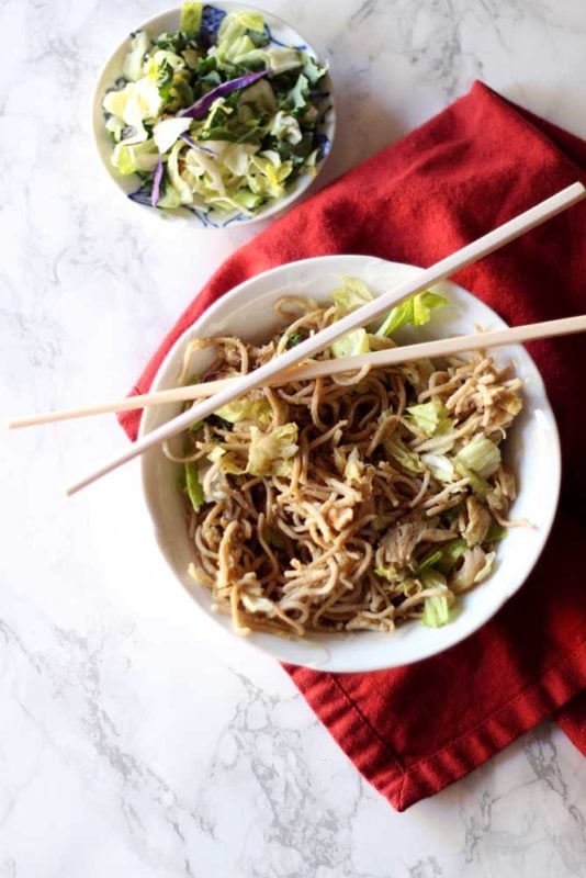 White bowl containing Thai Peanut Chicken Pasta, sitting on red napkin with cross chopsticks.