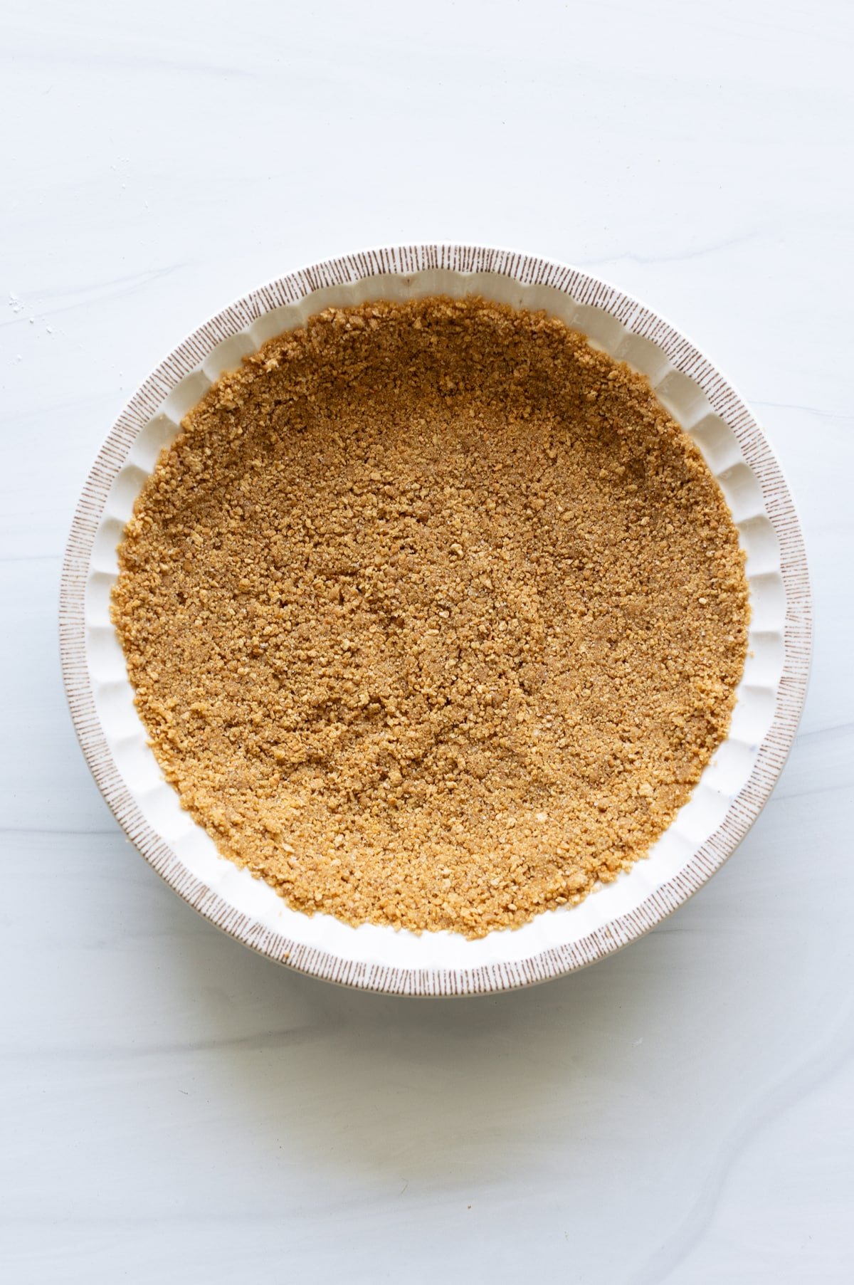 Person making a graham cracker crust and putting it in a pie dish. 