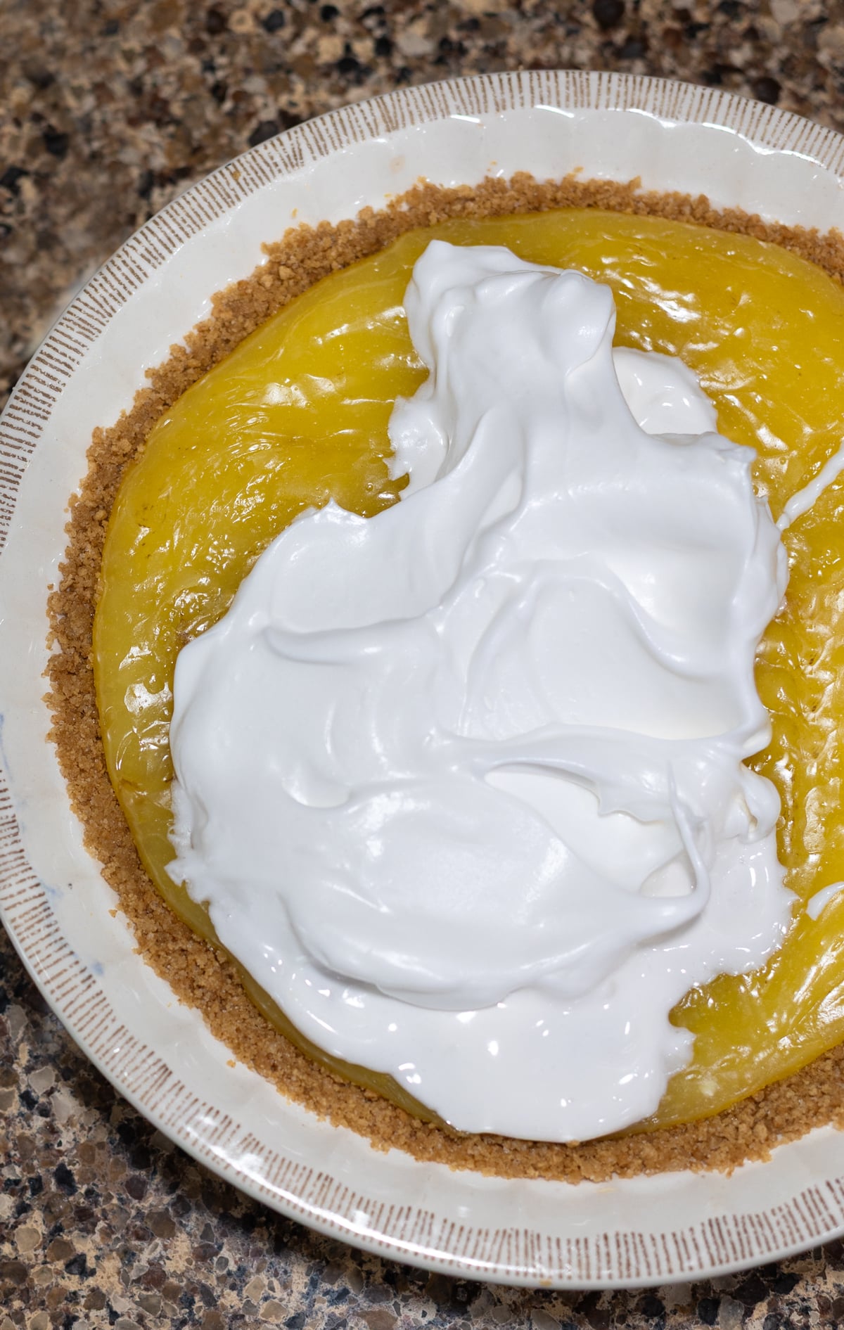 Person spreading meringue over lemon pie filling. 