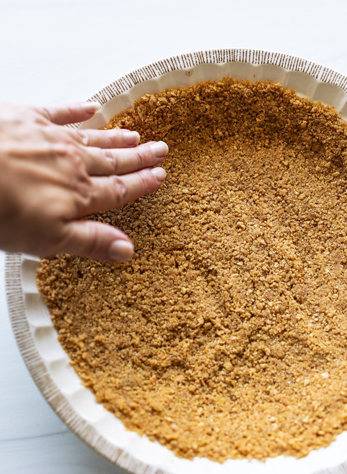Person pressing doen the graham cracker crust in the pie shell. 