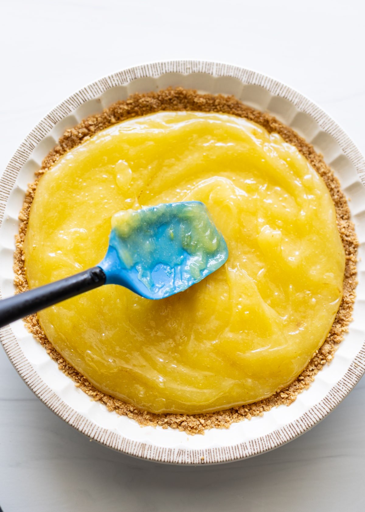 Person spreading lemon meringue over a graham cracker crust. 