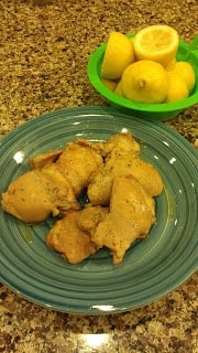 A green plate of cooked boneless skinless chicken thighs seasoned with lemon and garlic on a counter top.