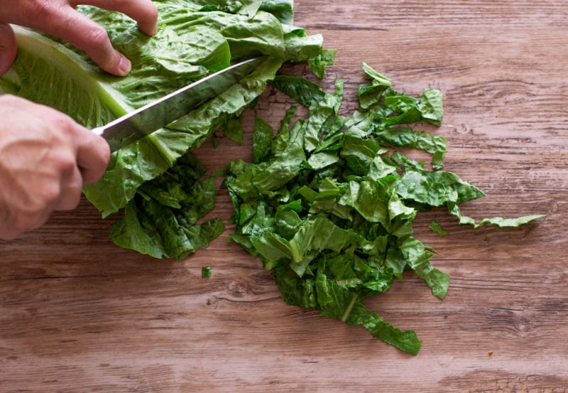 Person chopping romaine lettuce on wooden table.