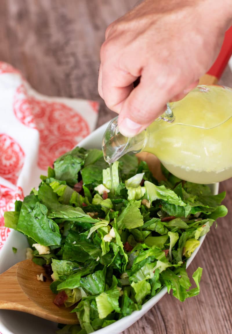 Vinaigrette dressing being poured on salad in a glass bowl.