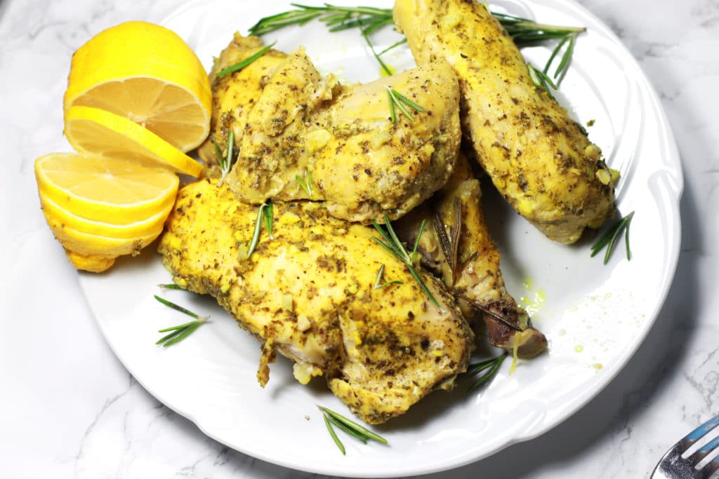 Pieces of chicken covered in sprigs of herbs with lemon slices on a white plate.