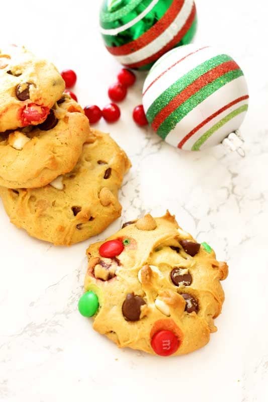 4 cookies sitting on a white marble table topped with M&Ms, Christmas calls on table with red cranberries.