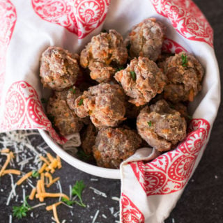 hite bowl containing cooked sausage balls, parsley and cheese on counter.