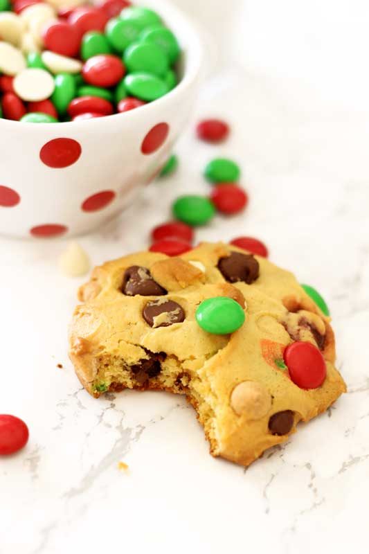 A boyfriend cookie with a bite taken out sitting on a white marble table, white and red polka dot dish filled with M&Ms on the side.