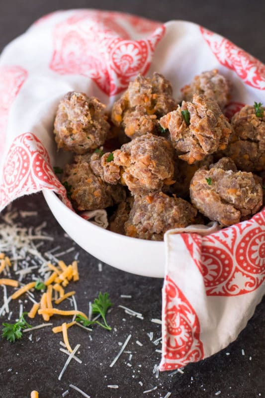 White bowl containing rolled balls of sausage and cheese, topped with fresh parsley.