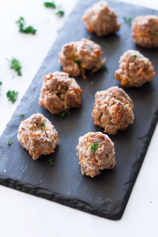 Black slate plate with 8 sausage balls topped with fresh parsley.