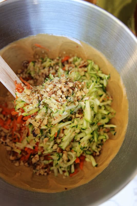 Mixing bowl containing wet and dry ingredients for the Carrot and Zucchini Bars, wooden spoon on side of bowl.