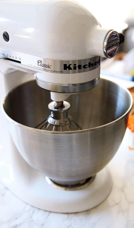 KitchenAid standing mixer with wire whisk sitting on a white marble table.