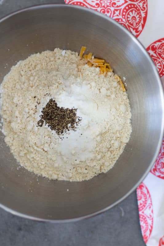 Silver bowl containing gluten free flour, baking soda, baking powder, sugar, salt, pepper and cheese.