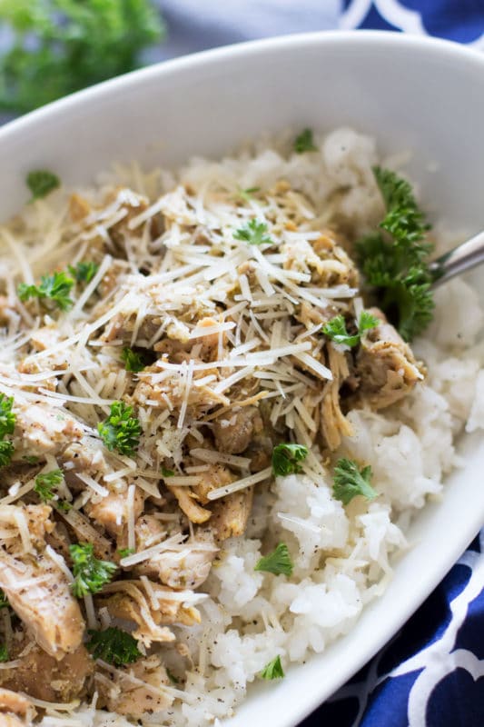 Chicken Pesto Thighs sitting in a white dish served over white rice topped with fresh parsley and Parmesan cheese.