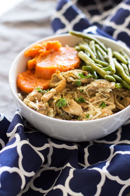 Pesto Chicken Thighs, sliced yams and green beans served in a white bowl, blue and white chevron napkin on table.