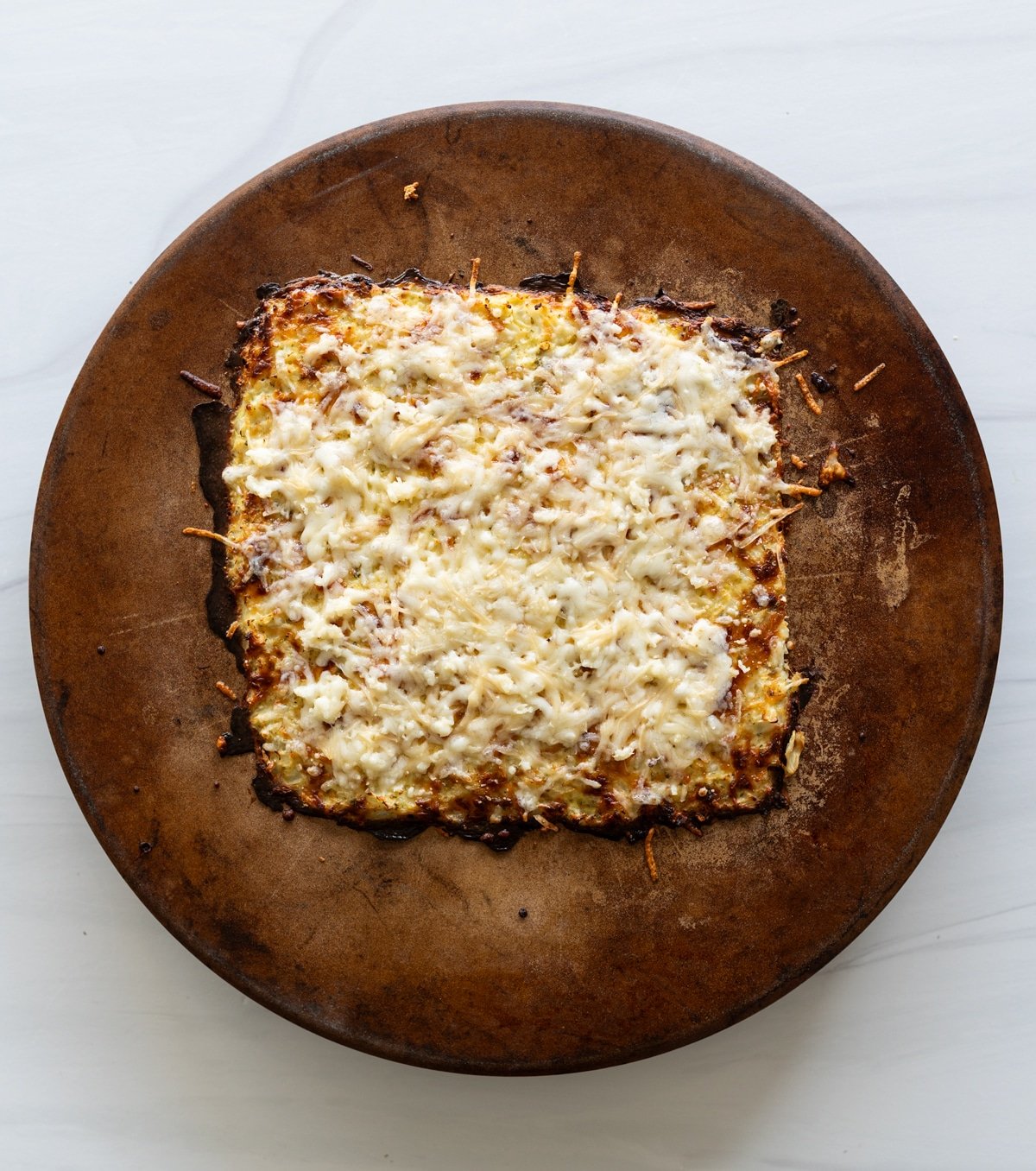 Person topping the cooked cauliflower breadsticks on a pizza stone 
