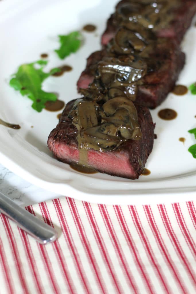 A close up of steak and mushrooms drizzled with a creamy balsamic mushroom sauce.