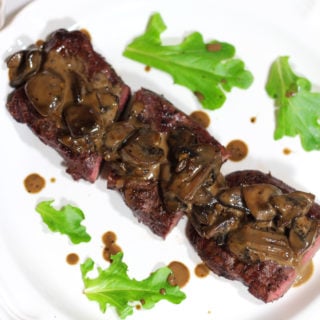 A close up of a white plate of steak and mushrooms drizzled with a creamy balsamic mushroom sauce.