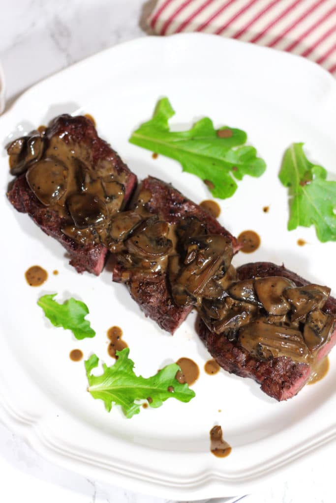 A close up of a white plate of steak and mushrooms drizzled with a creamy balsamic mushroom sauce.