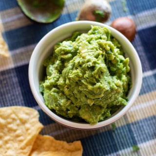 White bowl containing homemade guacamole, chips on table.