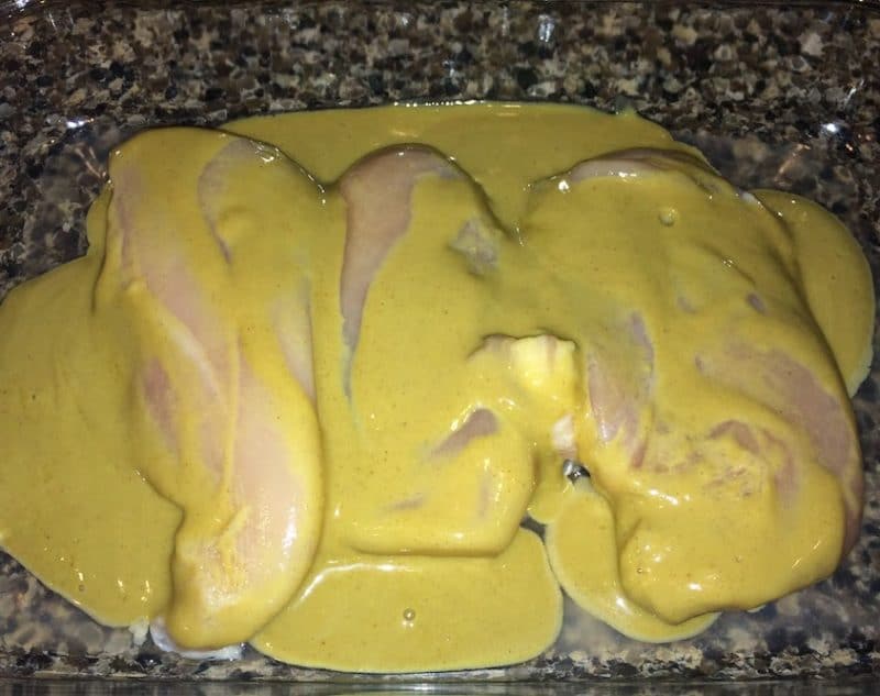 A pyrex pan of three uncooked chicken breast smothered with dijon mustard.
