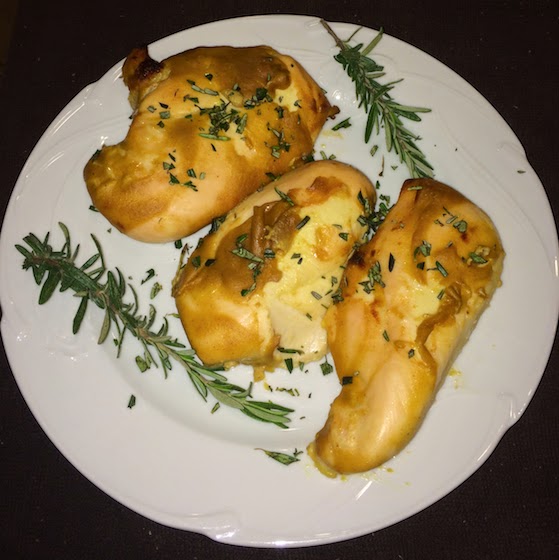 A white plate of three baked chicken breasts on a black table.