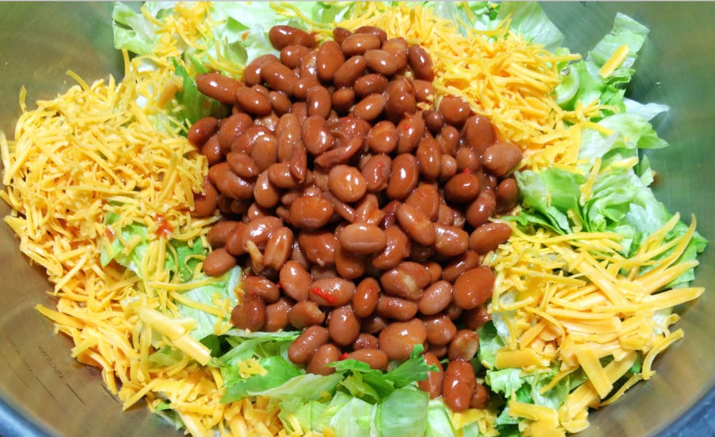 A close up of beans, shredded cheese, on a bed of chopped iceberg lettuce.