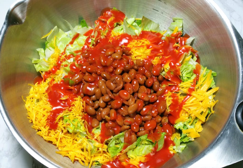 A bowl of beans, shredded cheese, on a bed of chopped iceberg lettuce cover with Catalina Dressing.