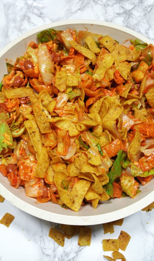 A bowl of corn chips, shredded cheese, chopped lettuce, beans all mixed with Catalina dressing.