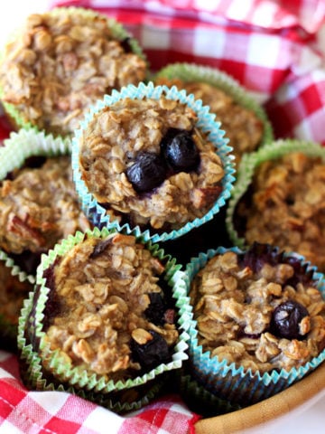 Brown bowl with a red and white checkered napkin containing 7 Baked Oatmeal Blueberry Oatmeal Cupcakes.