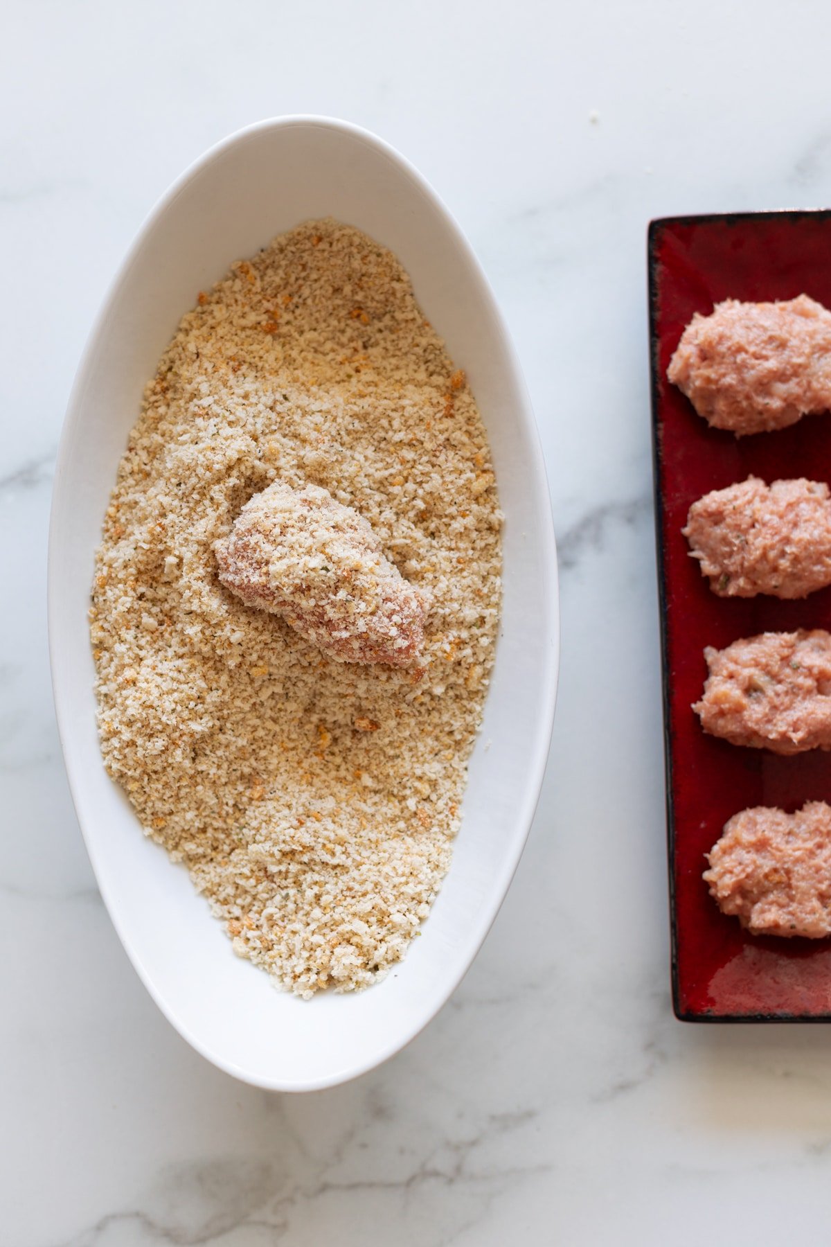 Raw turkey nuggets being dipped into breadcrumbs.