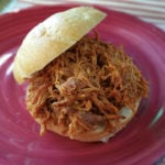 A red plate of pulled bar-b-que chicken on a kaiser roll.