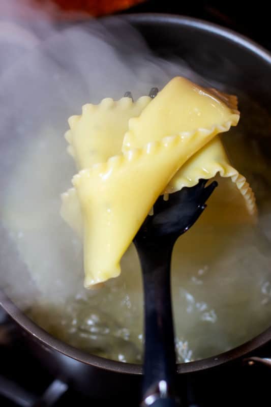 Cooked lasagna noodles draining from a pot of boiling water.