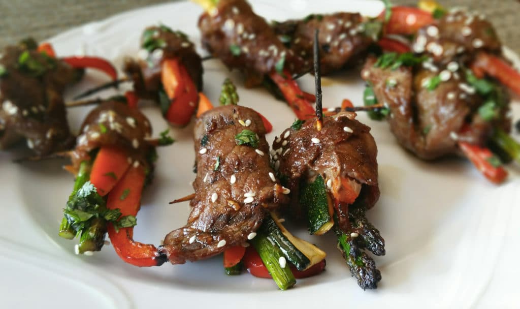 A plate of 7 Asian steak roll-ups containing asparagus and carrots