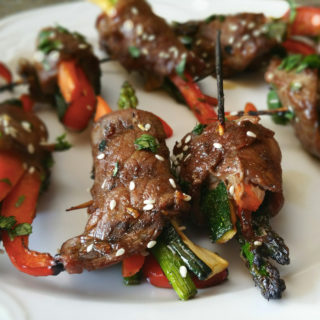 A plate of 7 Asian steak roll-ups containing asparagus and carrots