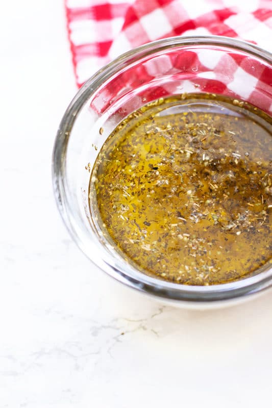 Glass bowl containing ingredients for Greek Dressing, olive oil, lemon juice, garlic, oregano, apple cider vinegar and dijon mustard.