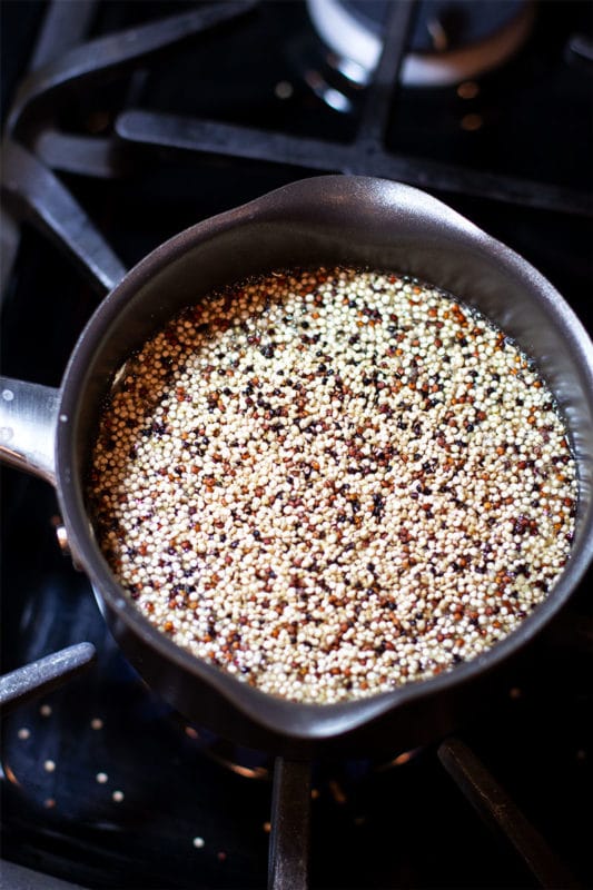 Pot containing red, black and white quinoa cooking on a stove.
