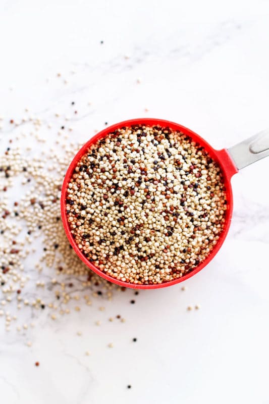 Raw tri-colored, red, black and white quinoa in a red measuring cup.