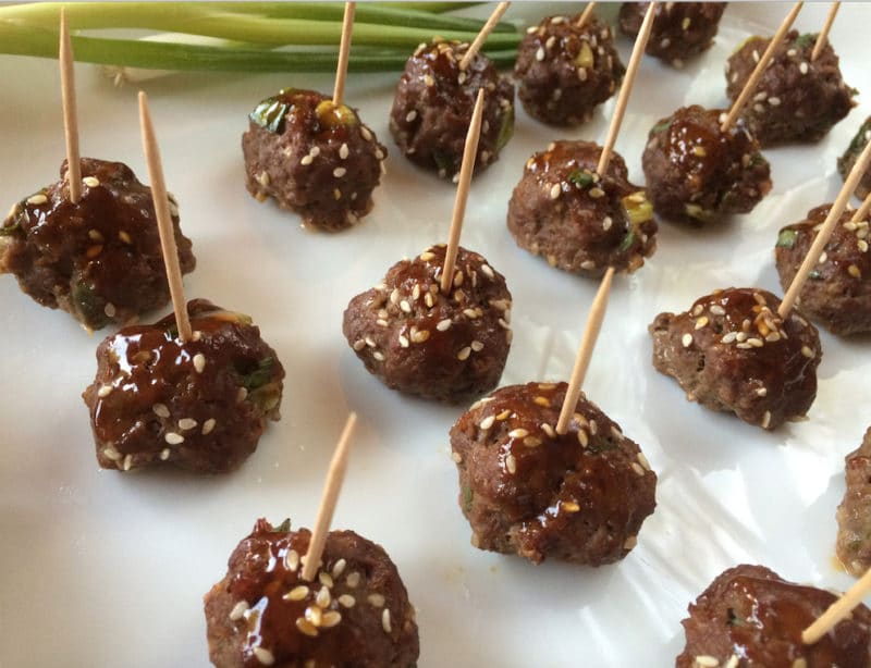 Rows of cooked meatballs with a tooth stuck in the top sprinkled with sesame seeds.