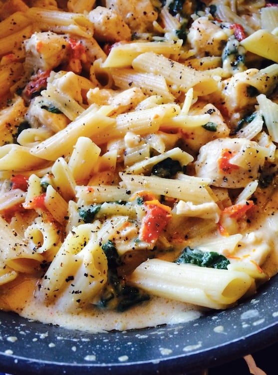 Blue plate containing Chicken Florentine with Sun Dried Tomato Pasta topped with melted cheese, spinach and fresh ground pepper.