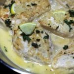 A close up of chicken smothered with a cream sauce and cut lemon on a plate.